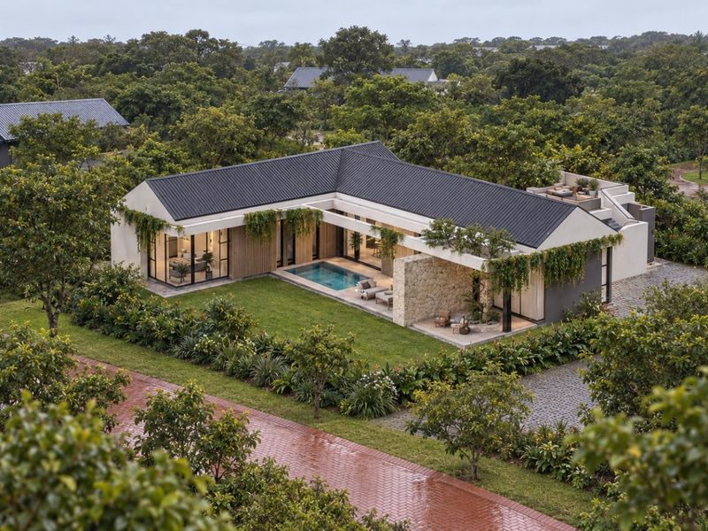 Aerial view of a modern L-shaped residence featuring a private swimming pool, covered patio, stone accents, and lush landscaped surroundings.