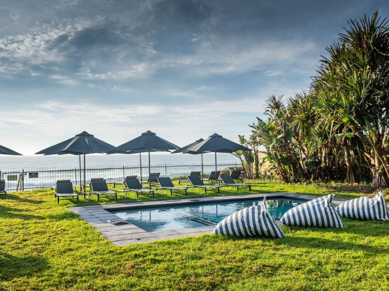 A well-maintained outdoor swimming pool area featuring stone coping, lush lawn, and scenic ocean views, perfect for relaxation.