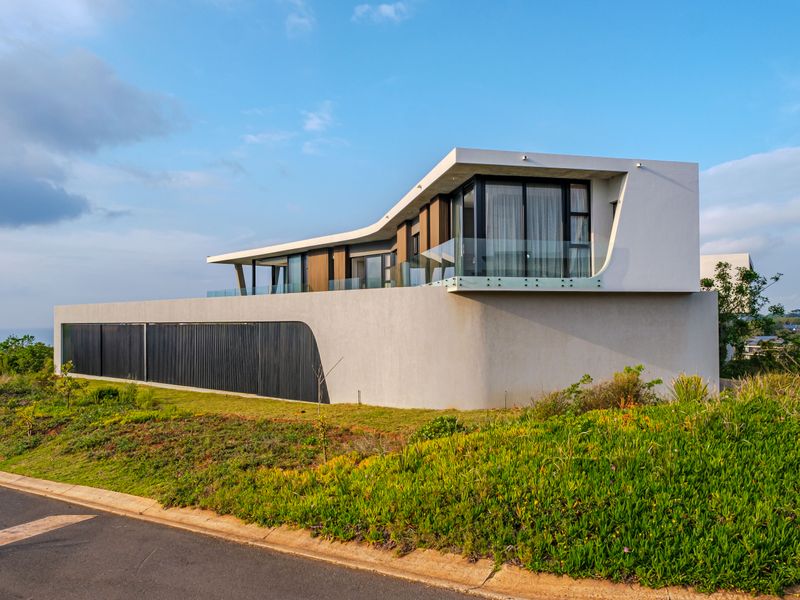 Modern architectural house featuring a striking curved concrete facade, cantilevered roof, and glass balustrades overlooking the landscape.