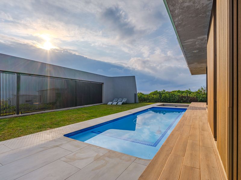 Modern outdoor pool area featuring a rectangular swimming pool, timber decking, tiled surround, and a contemporary slatted privacy screen.