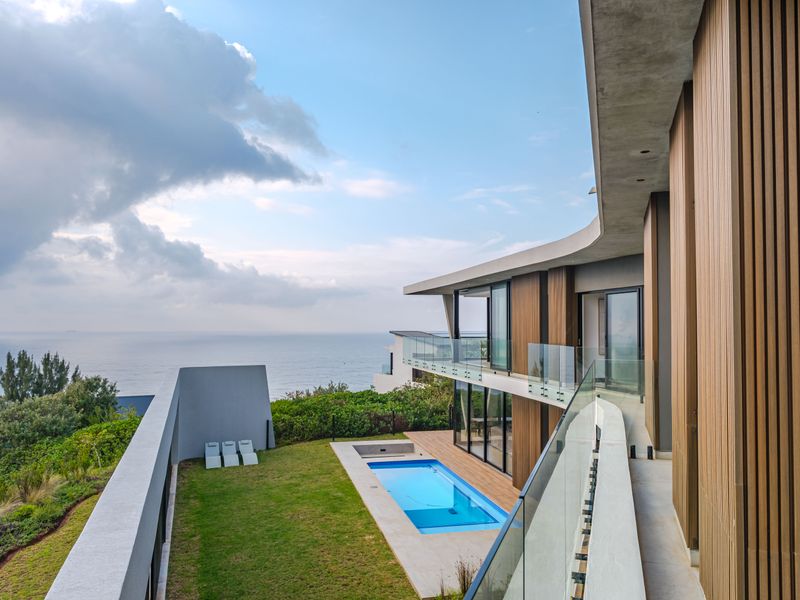 Modern architectural exterior featuring a swimming pool, glass balustrades, and timber-clad facade with expansive ocean views.