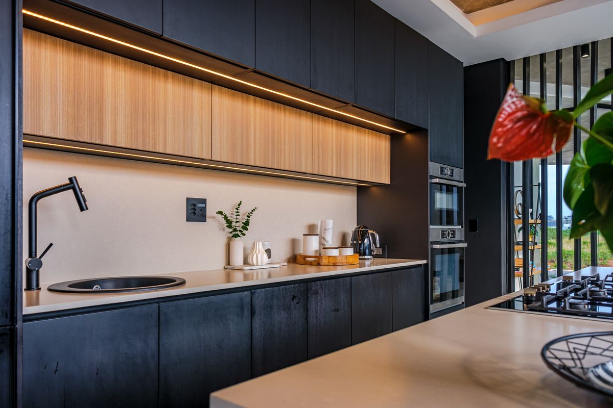 Modern kitchen featuring sleek dark cabinetry, wood-tone accents, integrated appliances, stone countertops, and high-end finishes with ambient under-cabinet lighting.