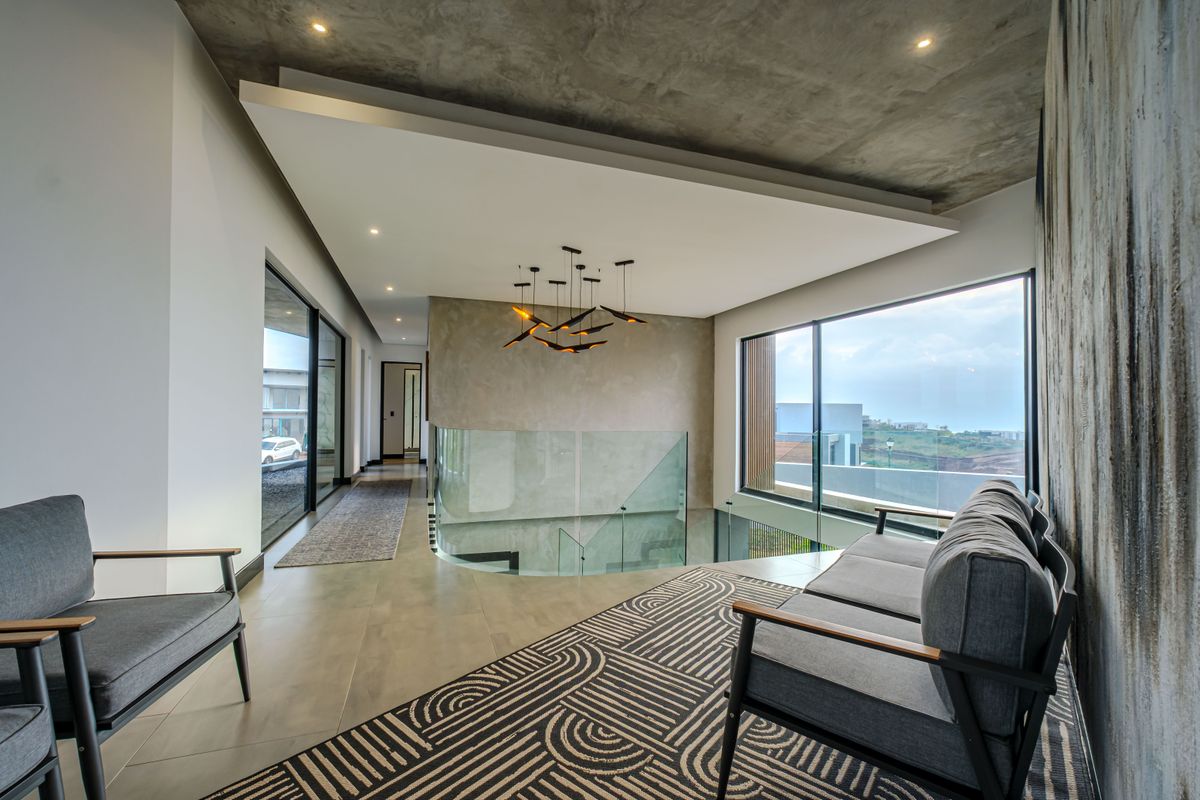 Modern living area featuring a concrete ceiling, glass balustrade, and large windows with views, showcasing high-end contemporary finishes and architectural design.