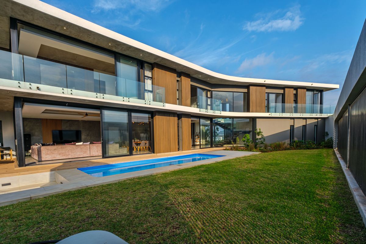 Modern two-story residence featuring a curved architectural design, integrated swimming pool, expansive glass sliding doors, and timber-clad facade overlooking a landscaped garden.