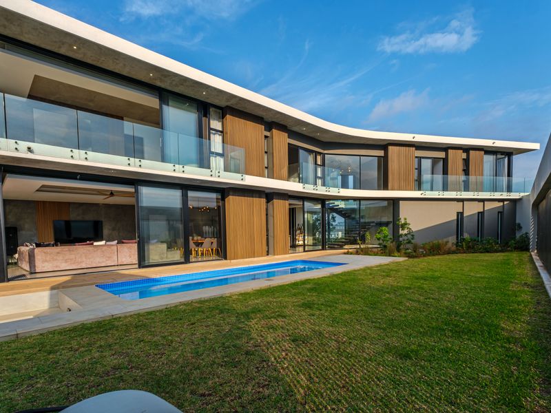 Modern two-story residence featuring a curved architectural design, integrated swimming pool, expansive glass sliding doors, and timber-clad facade overlooking a landscaped garden.