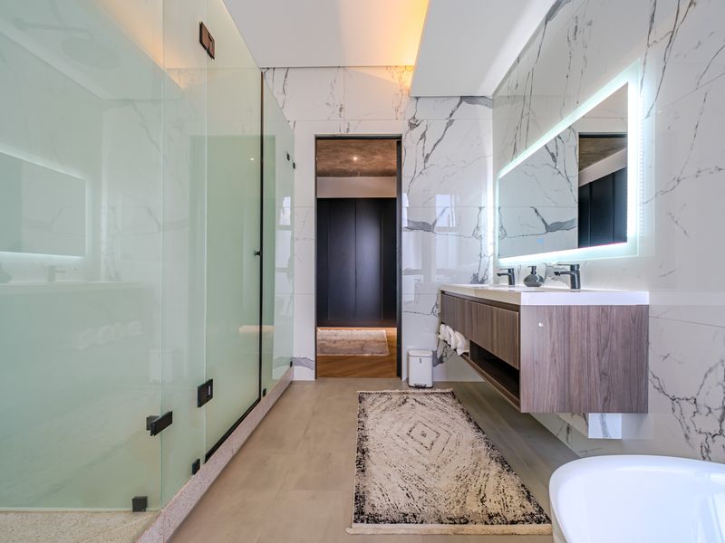 Modern luxury bathroom featuring a floating double vanity, backlit mirror, and a spacious walk-in shower with marble-look wall tiling.