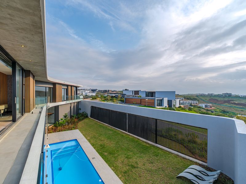 Modern outdoor living area featuring a swimming pool, glass balustrades, and a covered patio overlooking a landscaped garden and surrounding estate.