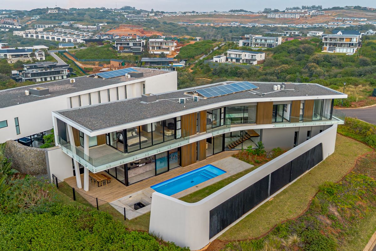 Aerial view of a modern multi-level residence featuring a swimming pool, solar panels, and expansive glass facades set within a landscaped estate.