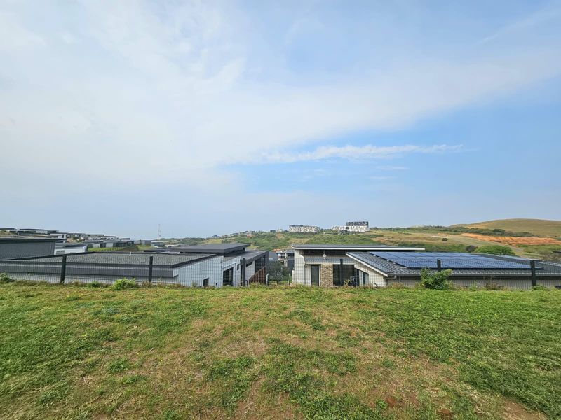A view from the vacant residential plot overlooking the surrounding estate, neighboring homes, and distant landscape.