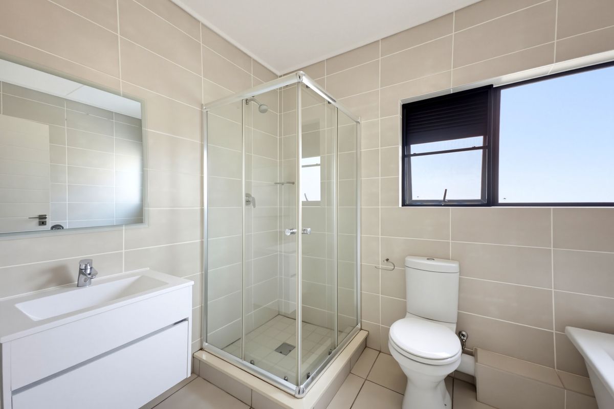 A modern, well-maintained bathroom featuring a glass shower enclosure, wall-mounted vanity with basin, and a toilet, finished with neutral floor-to-ceiling wall tiles.
