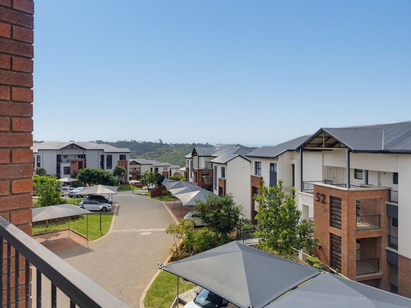 Elevated view overlooking a residential apartment complex with paved driveways, shade cloth carports, and modern brick and plaster building facades.