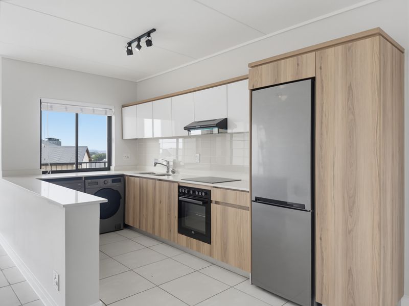 Modern kitchen featuring sleek wood-grain and white cabinetry, stone countertops, integrated appliances, and tiled flooring with ample natural light.