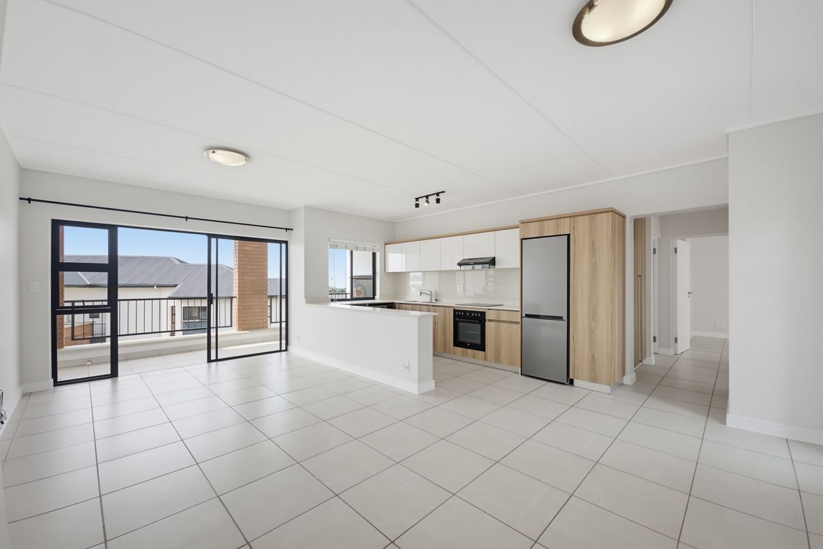 Spacious open-plan living and kitchen area featuring modern cabinetry, tiled floors, and large sliding doors leading to a private balcony.