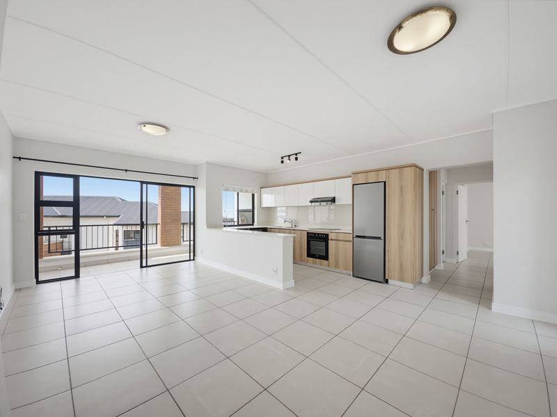 Spacious open-plan living and kitchen area featuring modern cabinetry, tiled floors, and large sliding doors leading to a private balcony.