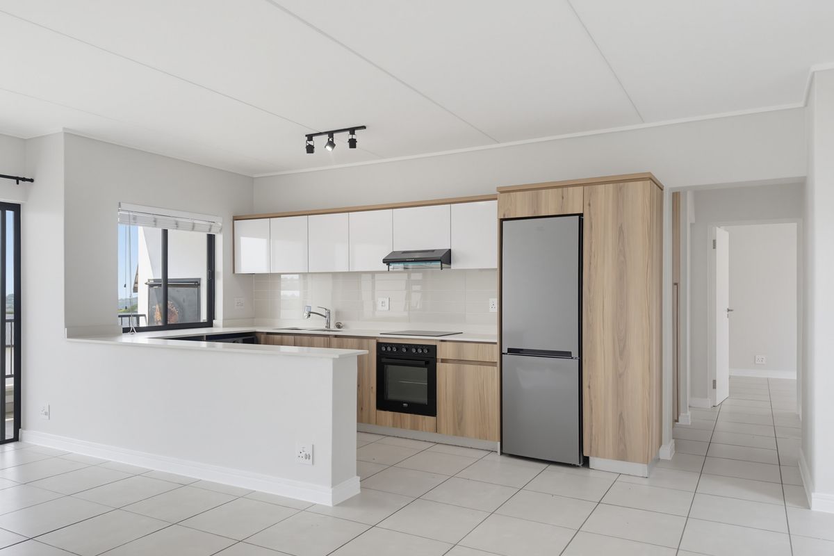 Modern open-plan kitchen featuring sleek white and wood-grain cabinetry, stone countertops, integrated appliances, and neutral tiled flooring in a well-maintained apartment.