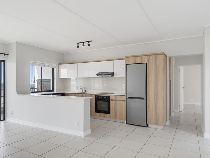 Modern open-plan kitchen featuring sleek white and wood-grain cabinetry, stone countertops, integrated appliances, and neutral tiled flooring in a well-maintained apartment.