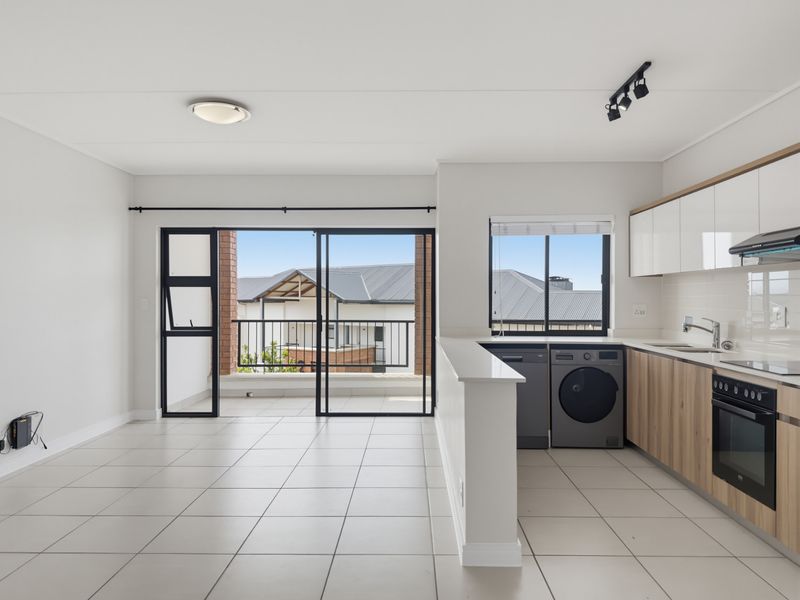 Modern open-plan kitchen and living area featuring tiled floors, sleek cabinetry, built-in appliances, and direct access to a private balcony.