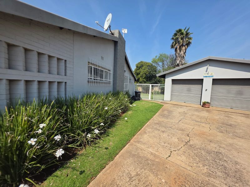 Front exterior view of the property featuring a double garage with roller shutter doors, a concrete driveway, and established garden beds.