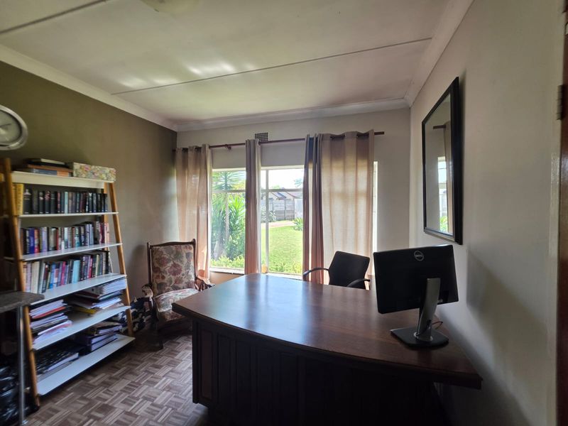 A functional home office space featuring parquet flooring, coved ceilings, and a large window providing natural light and garden views.