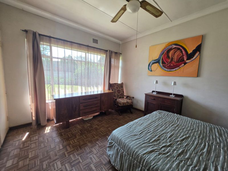 A spacious bedroom featuring classic parquet flooring, a ceiling fan, and a large window that allows for ample natural light.