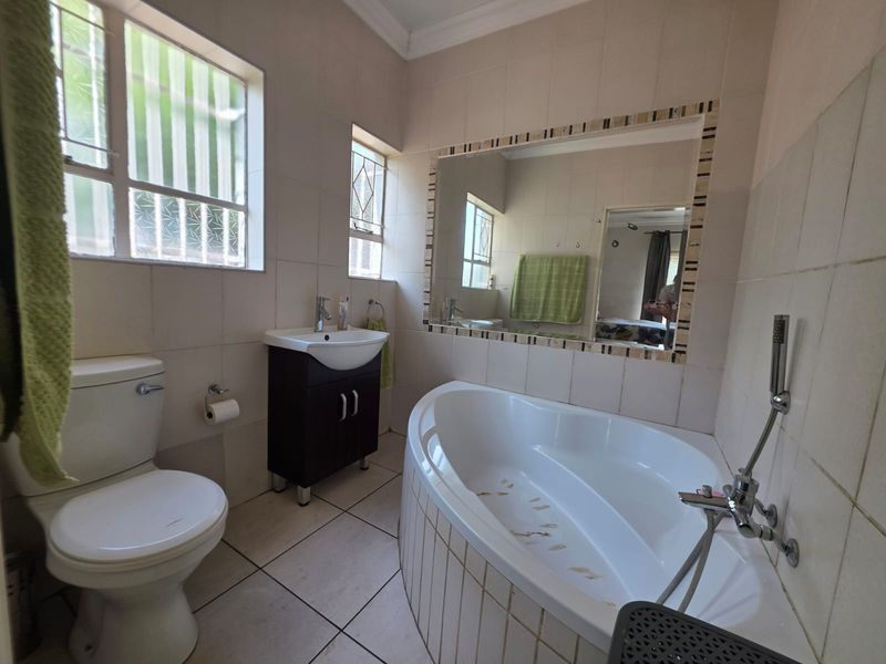 A functional bathroom featuring a corner bathtub, vanity cabinet with basin, and tiled finishes throughout.