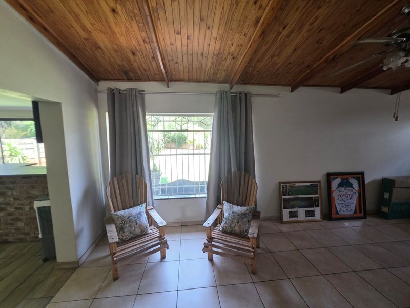 A living area featuring a warm timber-clad vaulted ceiling, ceramic floor tiles, and a window fitted with security burglar bars.