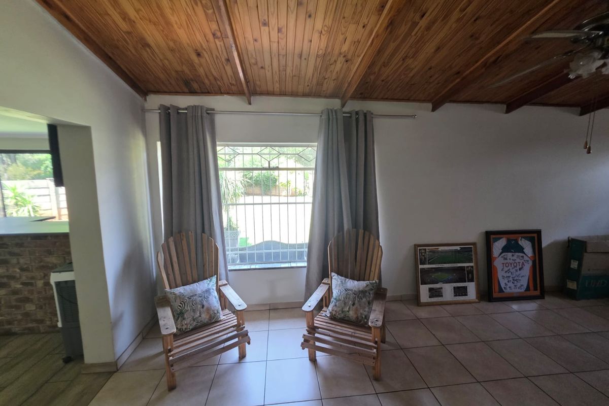 A living area featuring a warm timber-clad vaulted ceiling, ceramic floor tiles, and a window fitted with security burglar bars.