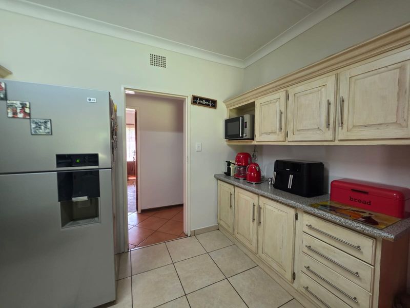 A functional kitchen featuring light-toned built-in cabinetry, granite-look laminate countertops, and tiled flooring, providing a practical workspace with direct access to the hallway.