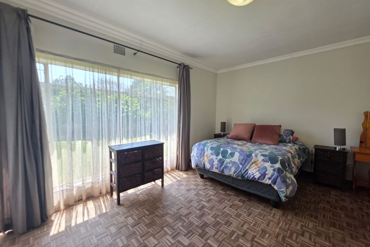 Spacious bedroom featuring classic parquet flooring, large windows allowing ample natural light, and neutral wall finishes.