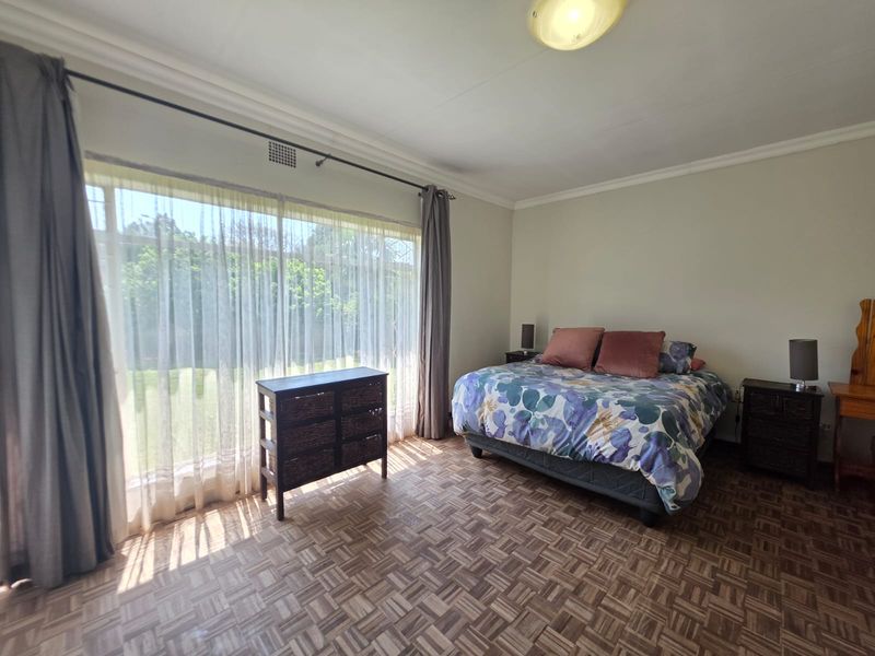 Spacious bedroom featuring classic parquet flooring, large windows allowing ample natural light, and neutral wall finishes.