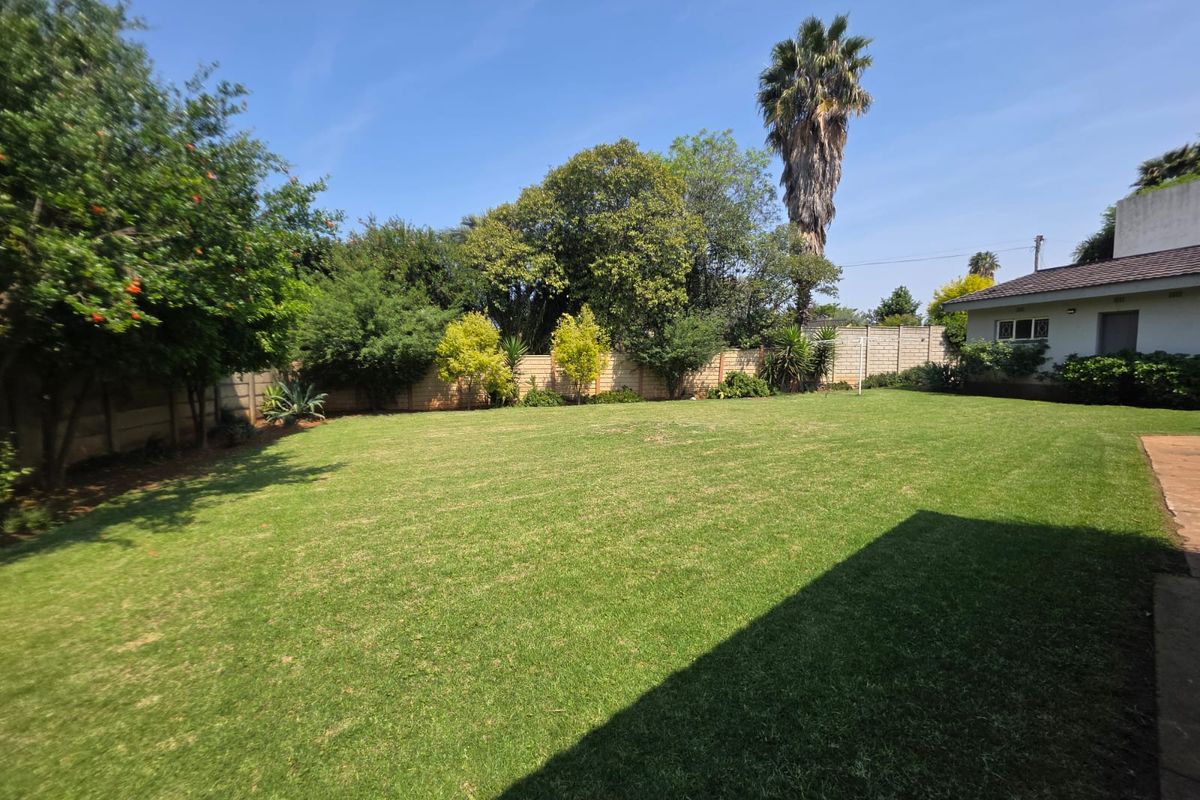 A spacious, well-maintained rear garden featuring a large lawn, mature trees, and a secure precast concrete boundary wall.