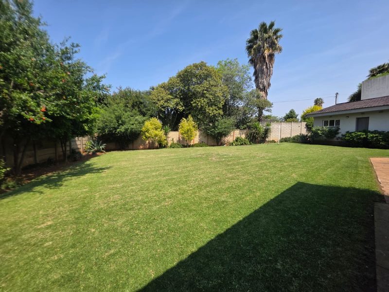 A spacious, well-maintained rear garden featuring a large lawn, mature trees, and a secure precast concrete boundary wall.