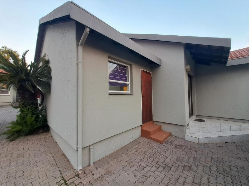 Rear exterior view of the townhouse featuring paved ground, tiled entrance steps, and a timber door with aluminium window frames.