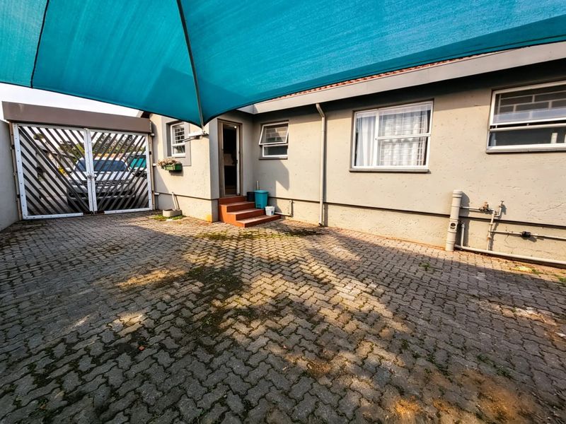 Rear exterior area featuring a paved courtyard, shade sail covering, and secure gated access to the property.