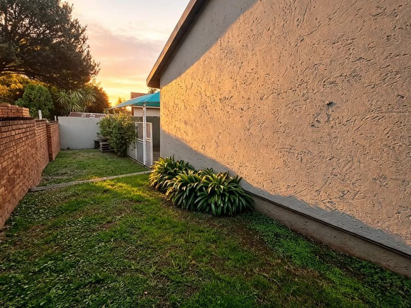 A view of the rear garden area featuring a textured exterior wall, a brick boundary wall, and a small lawn at sunset.