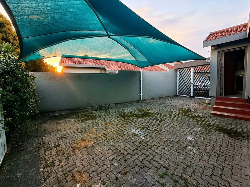 Rear exterior area featuring a paved driveway, shade sail covering, and secure boundary walling, providing a functional outdoor space.
