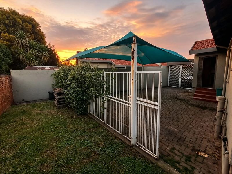 Rear exterior area featuring a paved driveway, metal security gate, and a shade sail structure set against a sunset backdrop.