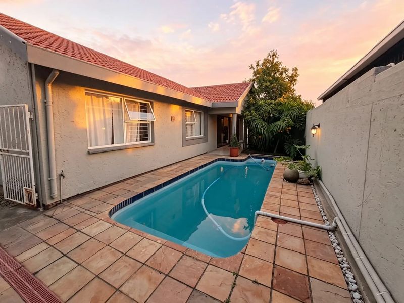 A private outdoor pool area featuring a tiled patio, terracotta roof tiles, and exterior wall lighting, set against the side of the townhouse.