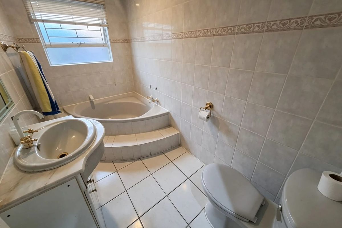 A functional bathroom featuring a corner bathtub, vanity basin, and toilet with neutral wall and floor tiling.