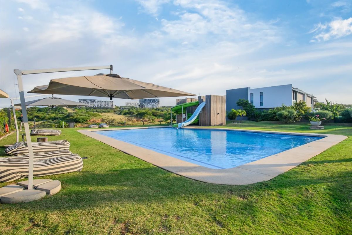 A well-maintained outdoor swimming pool area featuring a built-in water slide and expansive lawn, set against a scenic landscape.