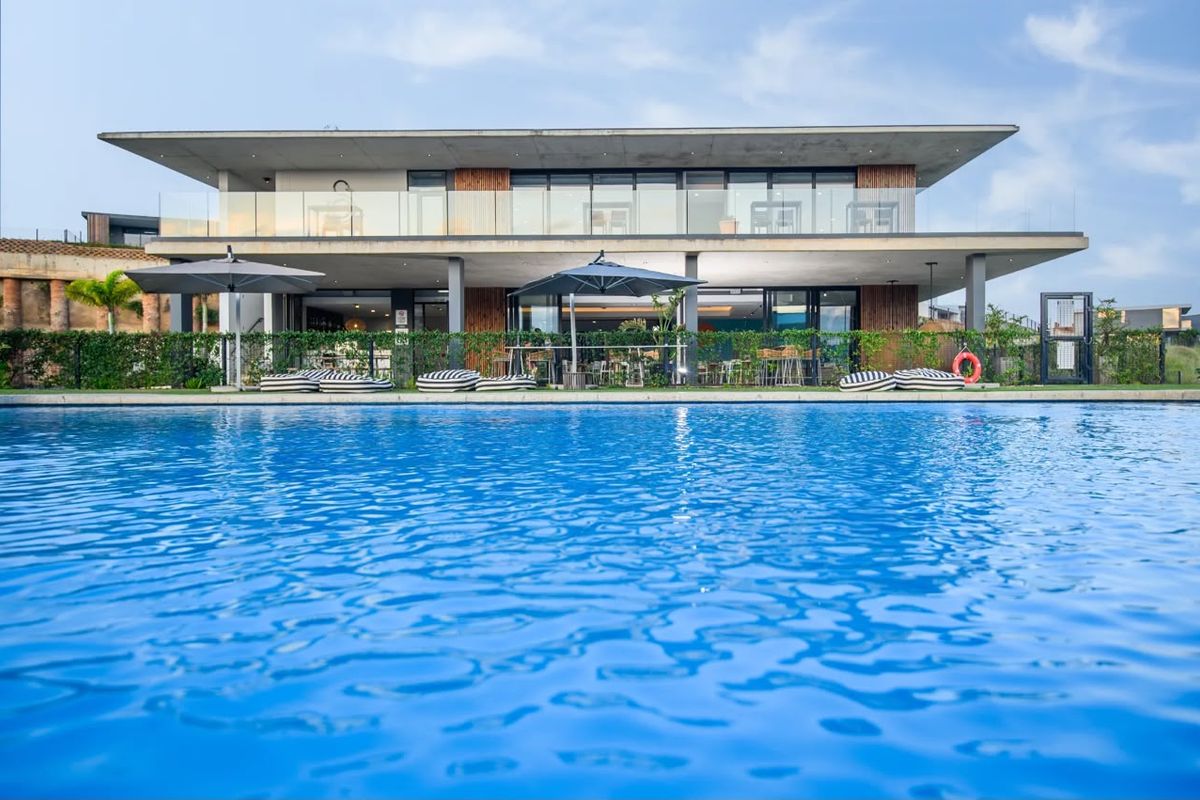 A modern two-story building featuring a large swimming pool in the foreground, glass balustrades, and a spacious covered patio area.