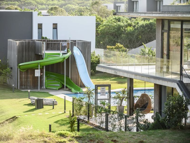 A well-maintained outdoor pool area featuring a modern water slide, timber-clad structure, and a glass-balustraded balcony overlooking the landscaped garden.