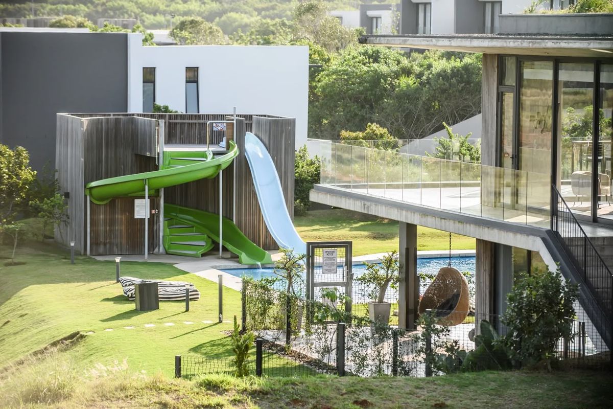 A well-maintained outdoor pool area featuring a modern water slide, timber-clad structure, and a glass-balustraded balcony overlooking the landscaped garden.