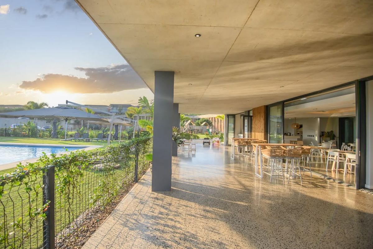 Spacious covered patio featuring polished concrete floors and recessed lighting, seamlessly connecting to the pool area and garden through large sliding glass doors.