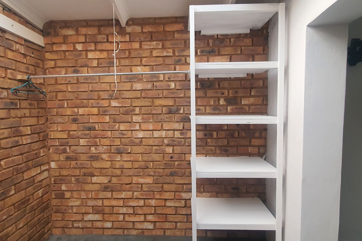 A bedroom walk-in closet area featuring exposed brick walls, built-in white shelving, and a hanging rail.