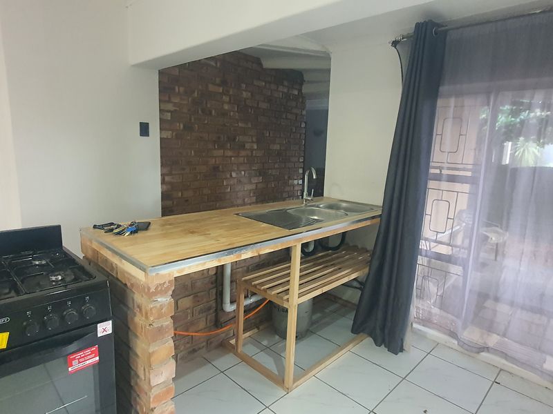 A compact kitchen area featuring a gas stove, brick-based island with a wooden countertop, stainless steel sink, and tiled flooring.