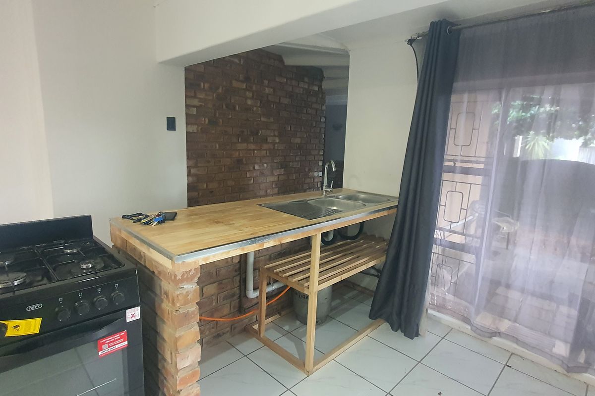 A compact kitchen area featuring a gas stove, brick-based island with a wooden countertop, stainless steel sink, and tiled flooring.