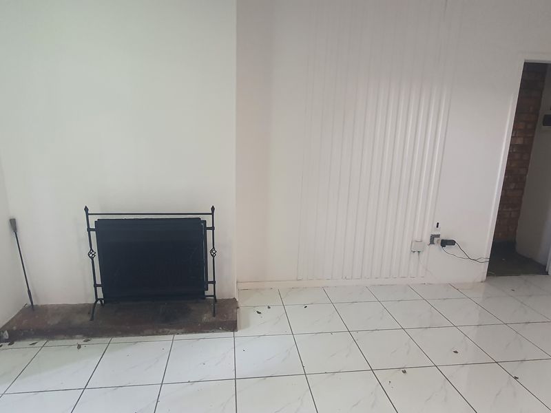 An empty living room featuring tiled flooring and a built-in fireplace, presenting a blank canvas for renovation and interior design.