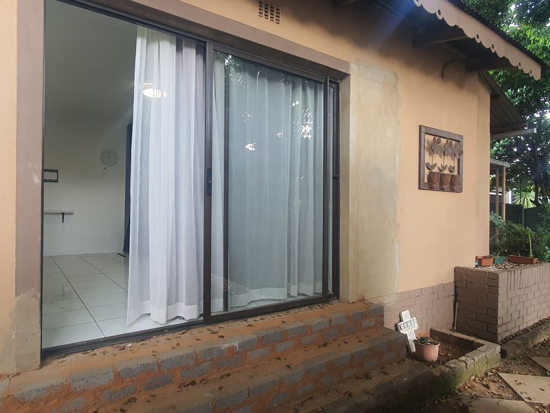 Rear exterior view of the property featuring a sliding glass door, brick steps, and a small brick planter box in the garden area.
