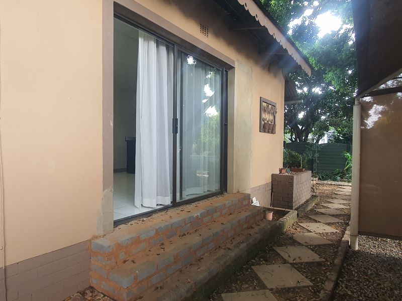 Rear exterior view of the property featuring a sliding glass door, brick steps, and a shaded outdoor area with a paved walkway.